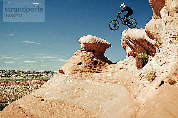 Mountainbiker springen von Klippe gegen Himmel