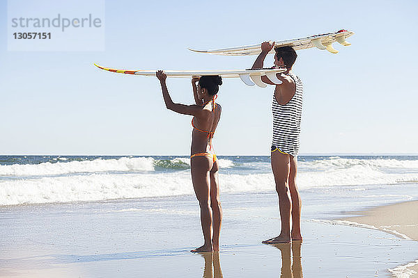 Paar  das am Strand stehend ein Surfbrett auf dem Kopf trägt