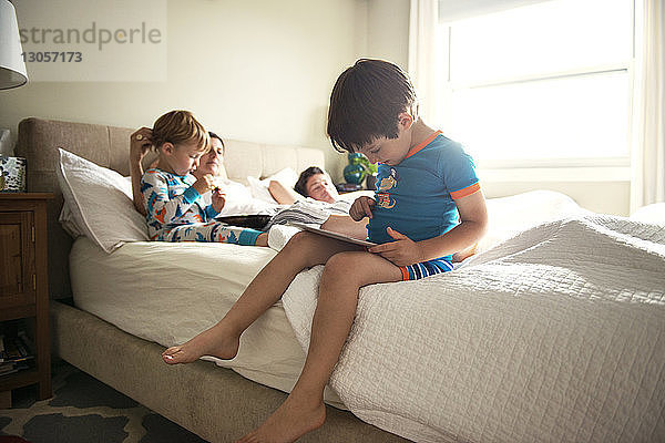 Junge benutzt Tablet-Computer  während die Familie zu Hause auf dem Bett liegt