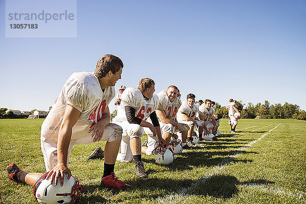 Glückliche Fussballmannschaft kniet auf Grasfeld gegen den Himmel