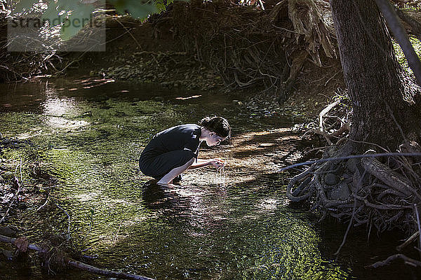 Seitenansicht eines Teenager-Mädchens  das Wasser hält  während es im Fluss kauert