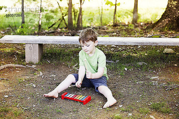 Hochwinkelansicht eines Jungen  der Spielzeug-Xylophon spielt  während er auf dem Spielplatz sitzt