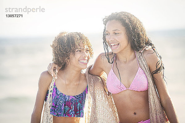 Fröhliche Freunde im Bikini am Strand spazieren