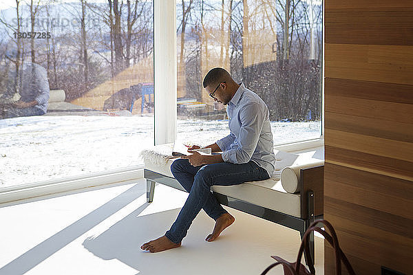 Seitenansicht eines Mannes  der Zeitung liest  während er zu Hause auf dem Sofa sitzt