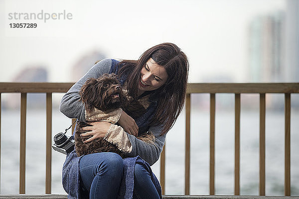 Frau sieht Hund an  während sie auf Bank am Hudson River sitzt