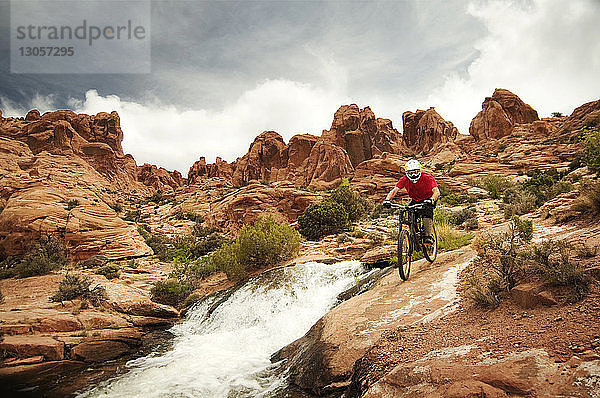 Mountainbiker radeln auf Felsen am Fluss gegen bewölkten Himmel