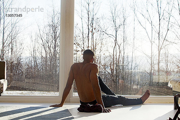 Rückansicht eines Mannes  der sich zu Hause am Fenster auf dem Boden entspannt