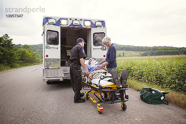 Patient liegt auf Krankenhausbahre von Sanitäter und Ehefrau auf Straße stehend
