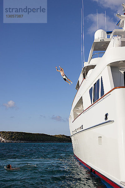Mann springt von Yacht  während Freund im Meer schwimmt