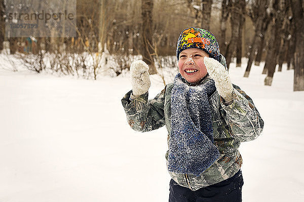 Glücklicher Junge spielt mit Schnee auf dem Feld
