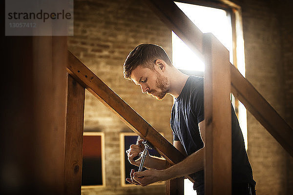 Seitenansicht des Mannes  der die Klemme an einem Holzgeländer zu Hause justiert