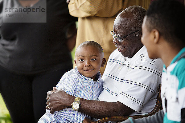 Glücklicher älterer Mann umarmt einen Jungen  während er mit seinem Enkel auf der Veranda sitzt