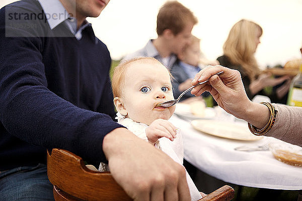 Ausgeschnittenes Bild einer Mutter  die ein Mädchen am Picknicktisch füttert