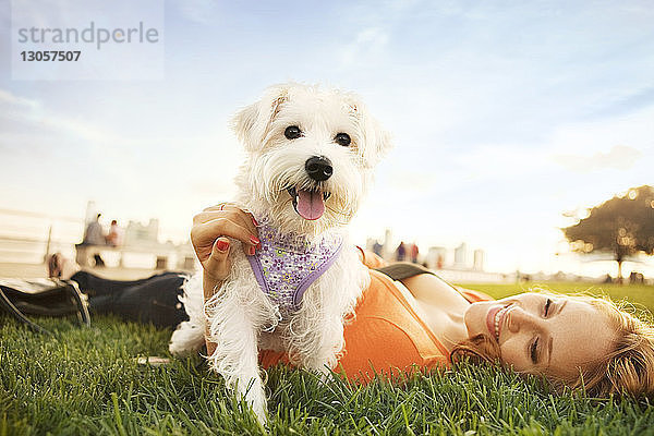 Frau liegt und spielt mit Hund auf Grasfeld
