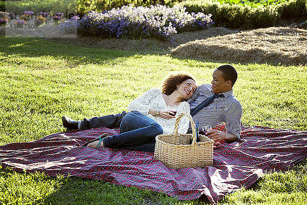 Glückliches Paar trinkt Wein  während es auf einer Picknickdecke auf einem Grasfeld liegt