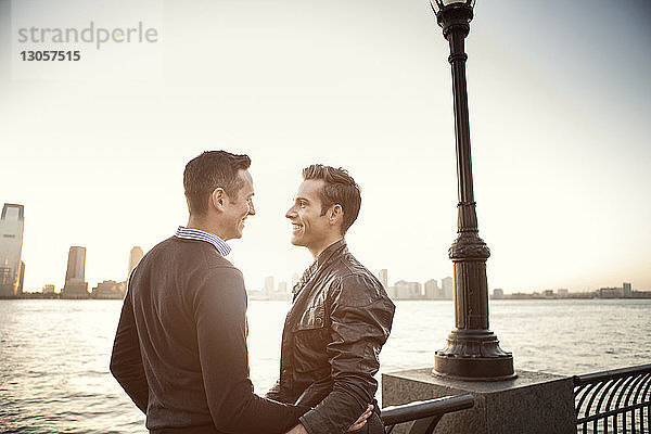 Glückliches homosexuelles Paar steht am Fluss gegen den Himmel