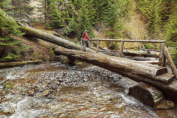 Frau steht auf Brücke über einen im Wald fliessenden Fluss