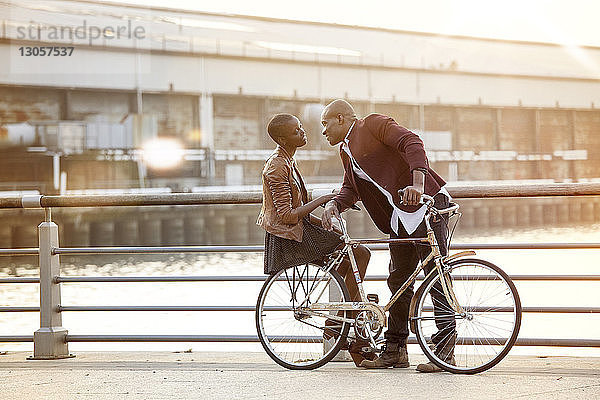 Mann schaut Frau in voller Länge an  die auf dem Fahrrad an der Reling gegen den Fluss sitzt