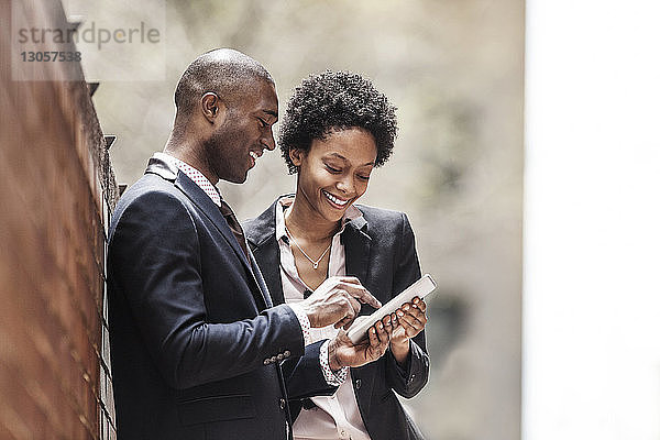 Glücklicher Geschäftsmann und Geschäftsfrau benutzen Tablet  während sie an der Wand stehen