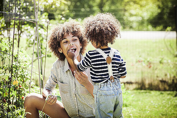 Junge  der seine Schwester im Garten mit Kirschtomaten füttert