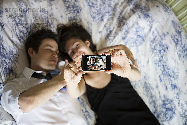Draufsicht eines glücklichen Paares  das im Bett liegend mit einem Smartphone fotografiert