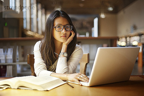 Porträt einer Frau  die einen Laptop benutzt  während sie in der Bibliothek sitzt