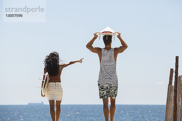 Frau zeigt auf eine Frau  während sie mit ihrem Freund am Strand steht