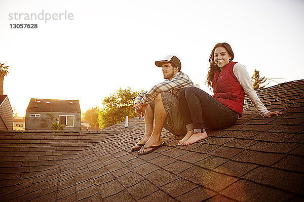 Glückliches Paar sitzt auf dem Dach vor klarem Himmel