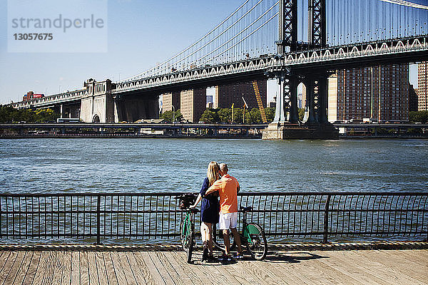 Rückansicht eines Paares mit Fahrrädern  das vor der Manhattan Bridge steht