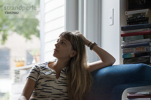 Nachdenkliche Frau sitzt zu Hause auf dem Sofa am Fenster