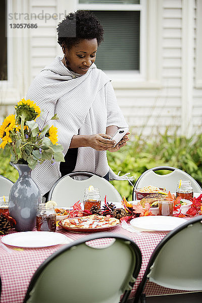 Frau fotografiert Essen durch Telefon am Tisch im Hinterhof