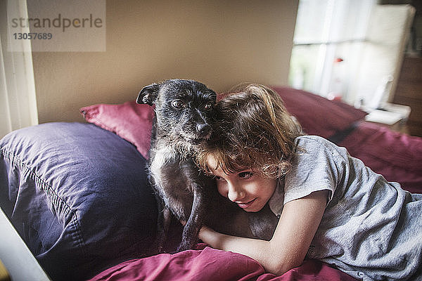 Mädchen umarmt Hund  während sie zu Hause auf dem Bett liegt