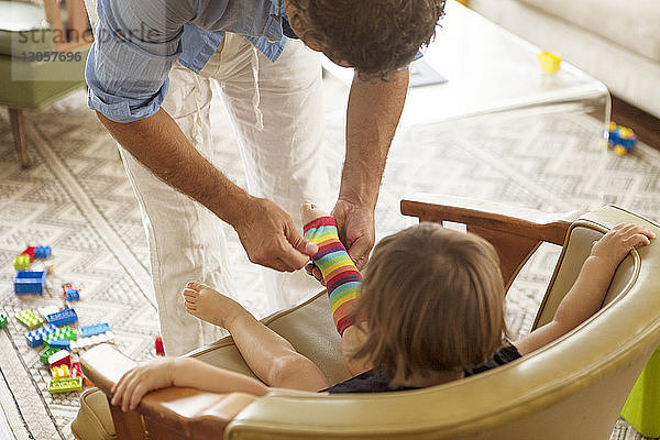 Schrägaufnahme eines Vaters  der einem Mädchen zu Hause beim Tragen von Socken hilft