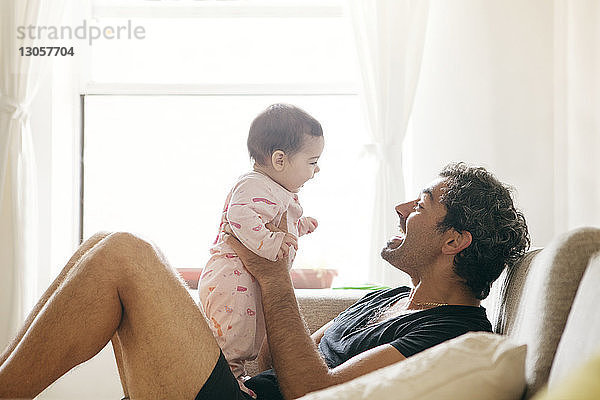 Seitenansicht eines Vaters  der mit seiner Tochter spielt  während er zu Hause auf dem Sofa sitzt