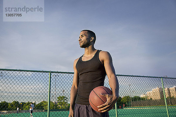 Nachdenklicher Sportler mit Basketball steht vor Gericht gegen den Himmel