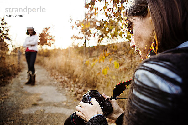 Frau betrachtet Fotos in Digitalkamera  während ein Freund auf einem Fußweg posiert