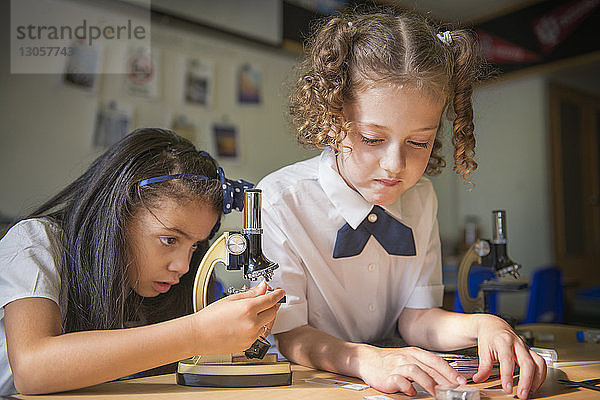 Mädchen benutzt Mikroskop von Freundin am Tisch im Labor