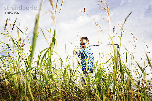 Selbstbewusster Mann spielt Golf auf dem Feld gegen den Himmel