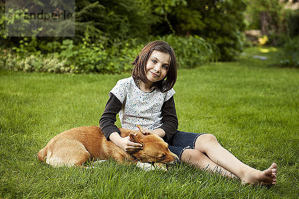 Bildnis eines Mädchens mit Hund auf einem Grasfeld im Hof sitzend