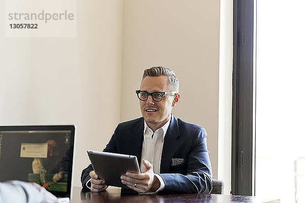 Geschäftsmann hält Tablet-Computer in der Hand  während er im Büro am Tisch sitzt
