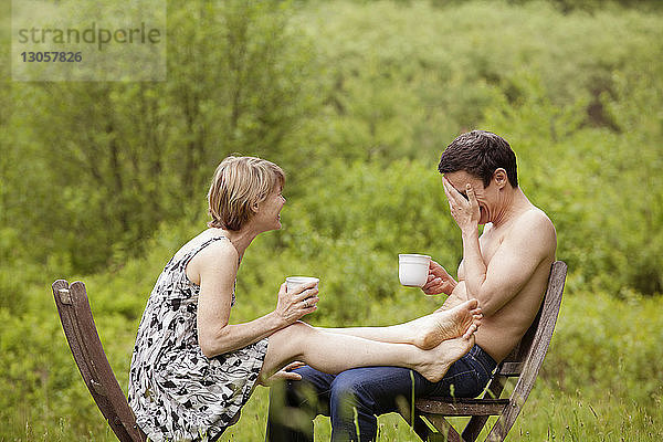 Paar  das Kaffeetassen hält  während es auf einem Stuhl im Feld sitzt
