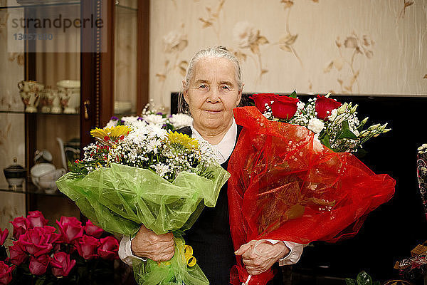 Porträt einer älteren Frau  die Blumensträuße hält  während sie zu Hause steht