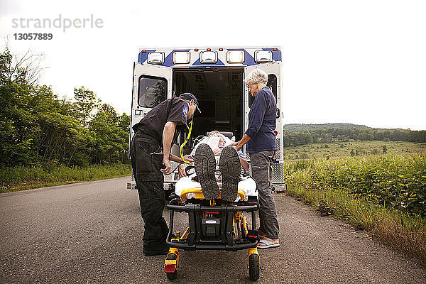 Sanitäter und Frau  die auf einer Krankenhausbahre liegend beim Patienten stehen