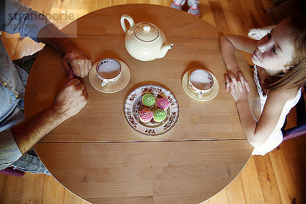 Draufsicht auf Vater und Tochter am Tisch sitzend mit Törtchen und Tee