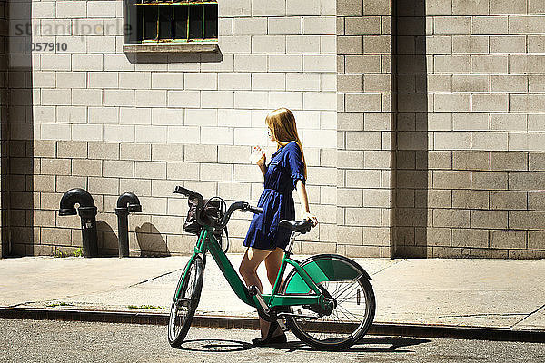 Seitenansicht einer Frau mit Fahrrad  die gegen ein Gebäude in der Stadt steht