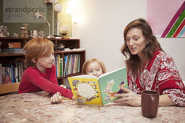 Mutter und Söhne lesen zu Hause bei Tisch Buch