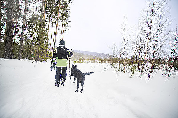 Rückansicht eines Jungen mit Hund beim Spaziergang auf schneebedecktem Feld gegen den Himmel