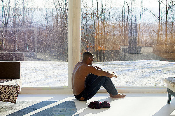 Mann sitzt zu Hause auf dem Boden am Fenster