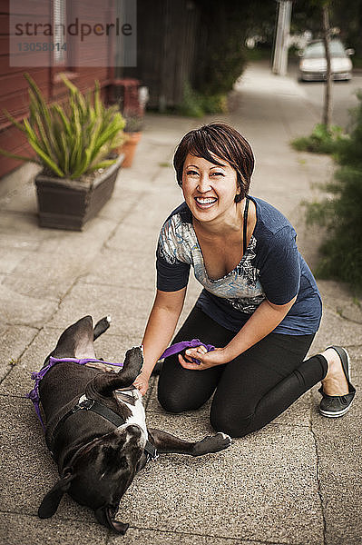 Porträt einer Frau  die mit einem Hund auf einem Fußweg spielt