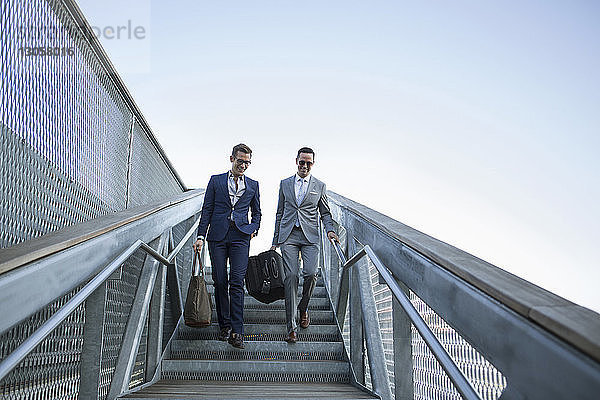 Geschäftsleute tragen Gepäck  während sie sich auf einer Treppe gegen den klaren Himmel nach unten bewegen